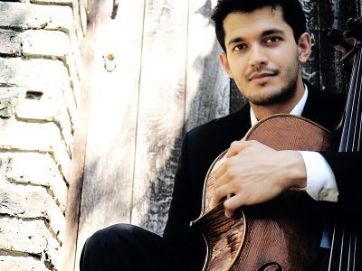 Ashok Klouda sits holding a violin. He has a smile across his face